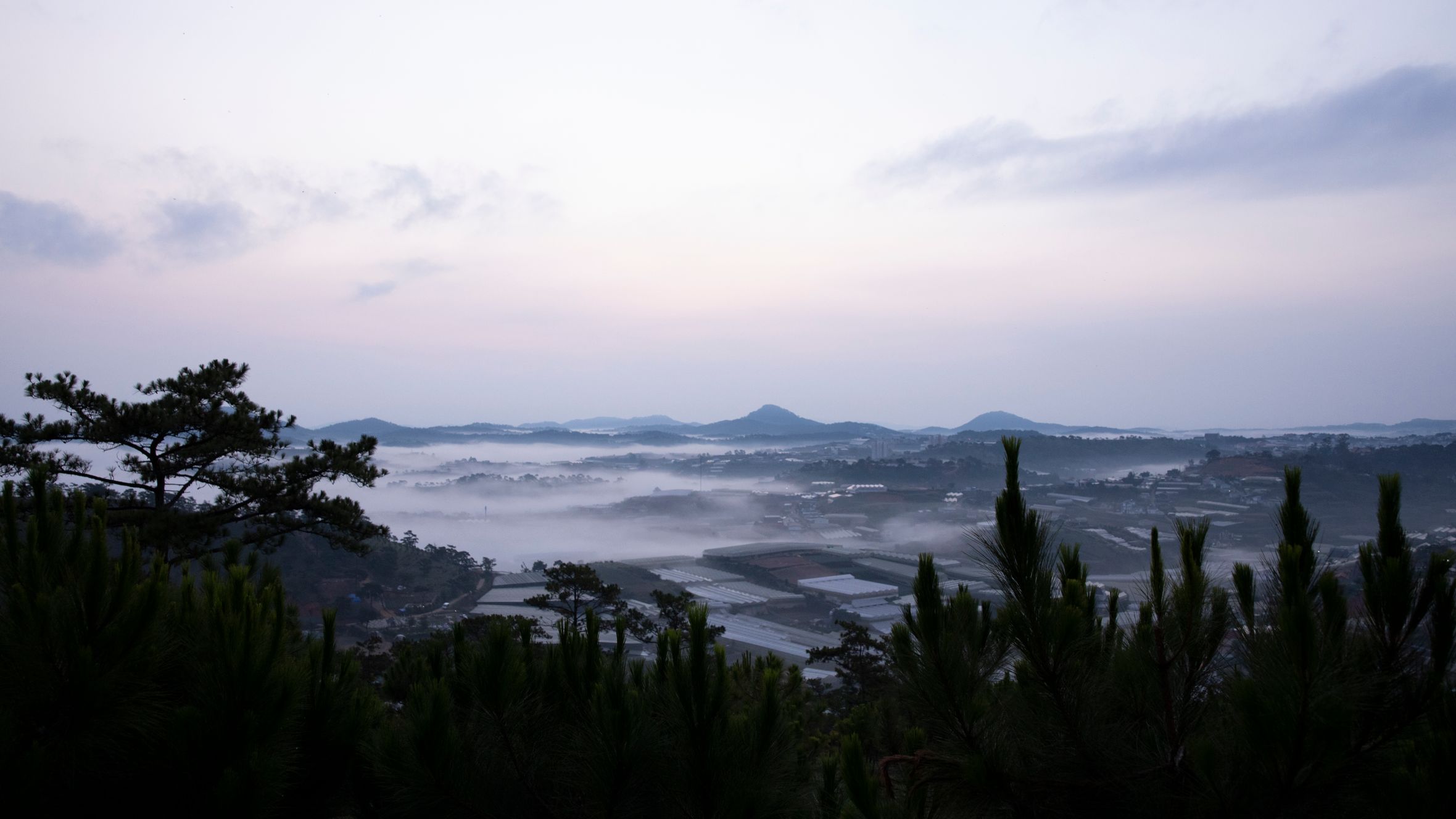 A tranquil valley landscape enveloped in morning mist with distant hills.
