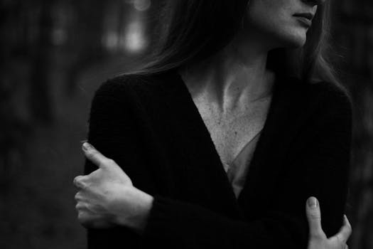 Artistic black and white portrait of a woman with embracing pose and contrast.