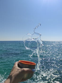 Hand holding cup with water splash against Sevastopol's sparkling sea during daytime.