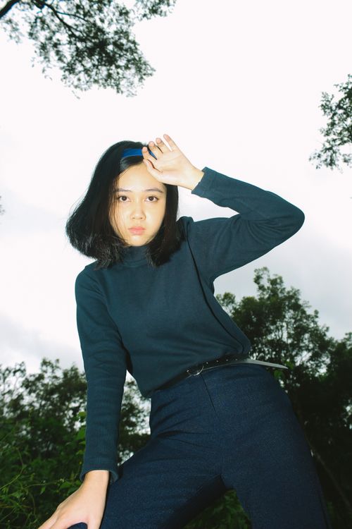 Free Low angle portrait of a young Asian woman in a dark outfit with hand on forehead outdoors. Stock Photo