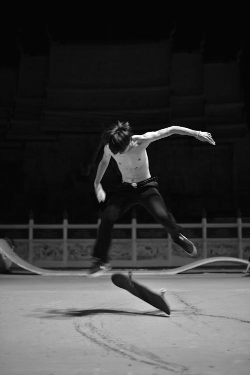 Grayscale Photo of a Man Doing a Skateboard Trick