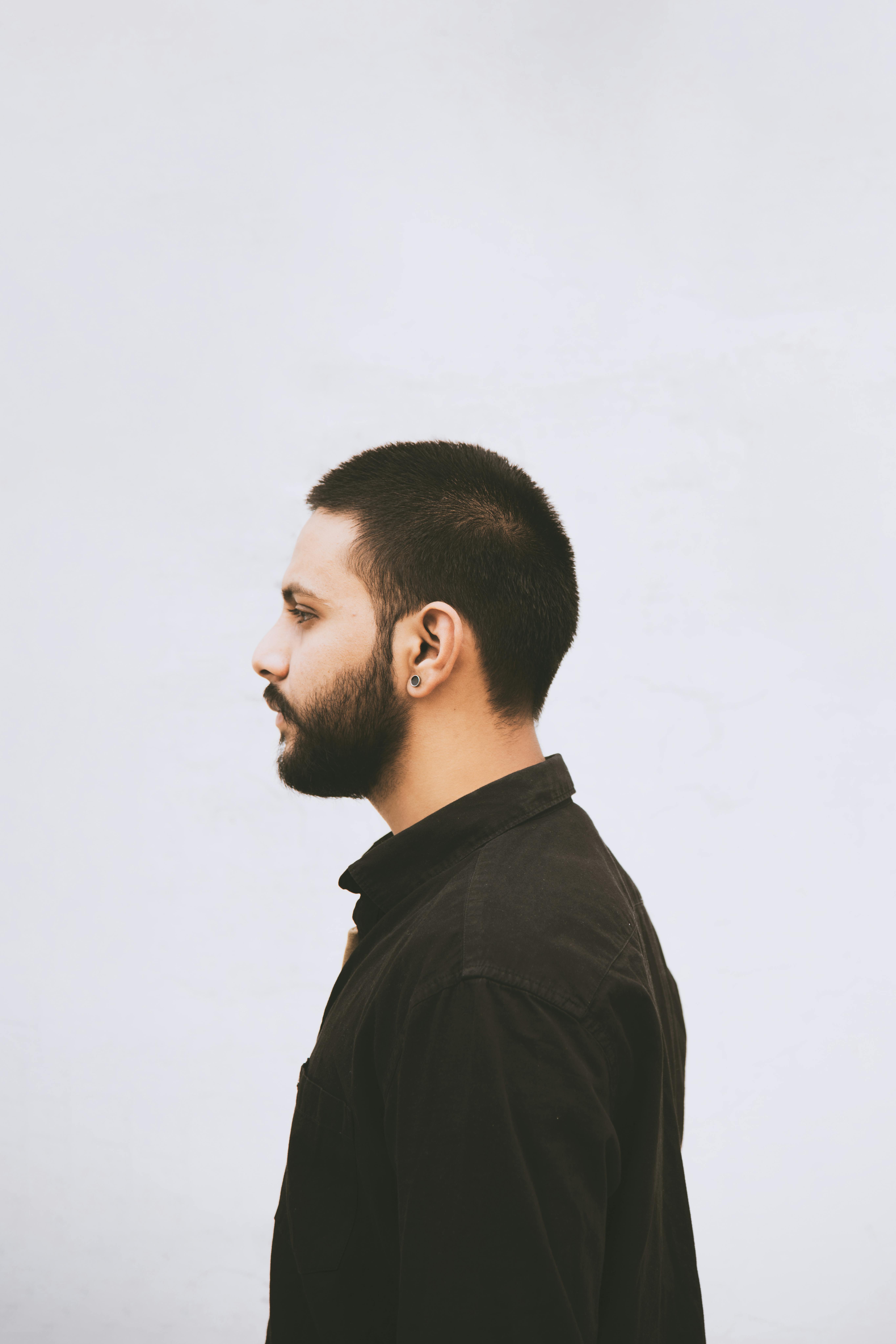 Side view of a man with a beard in a black shirt against a white background.