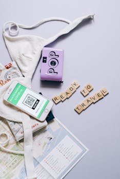Flat lay of travel essentials including smartphone, health passport, map, and scrabble tiles with 'Ready to Travel'.