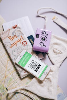 A collection of travel items including a smartphone showing a COVID-19 health passport, a camera, and a map.