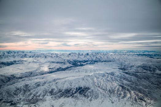 Scenic aerial view of a vast snowy mountain range with a cloudy sky during winter season.