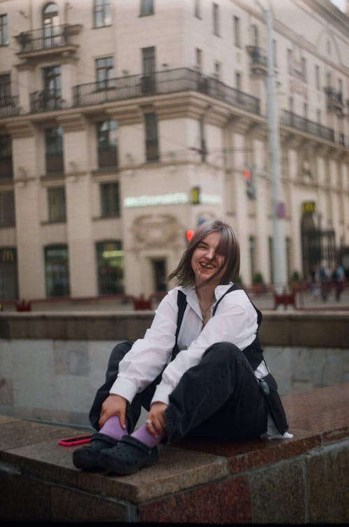 Smiling Woman Sitting on Marble Fence in City