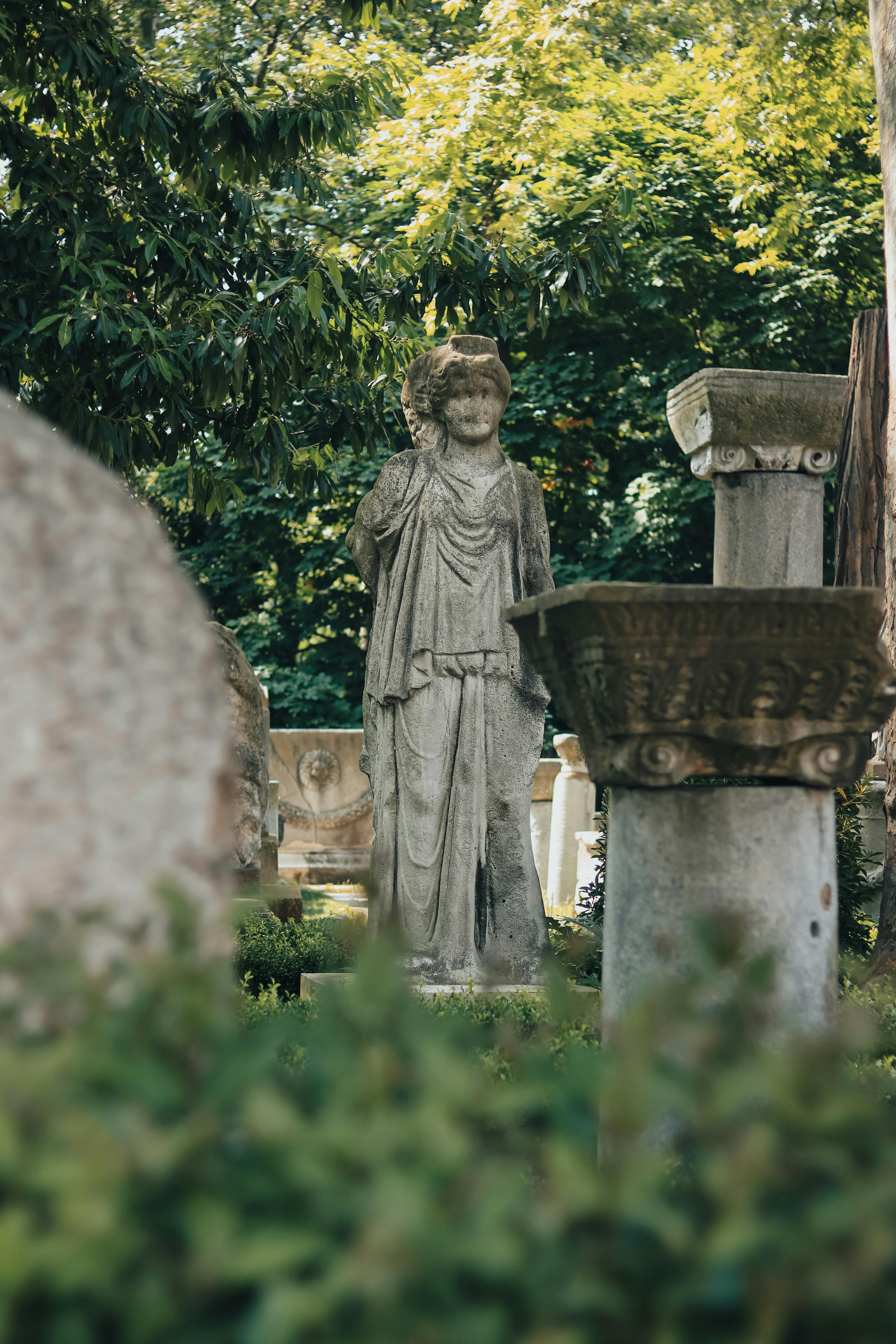 Elegant stone statue surrounded by greenery in a serene park setting.