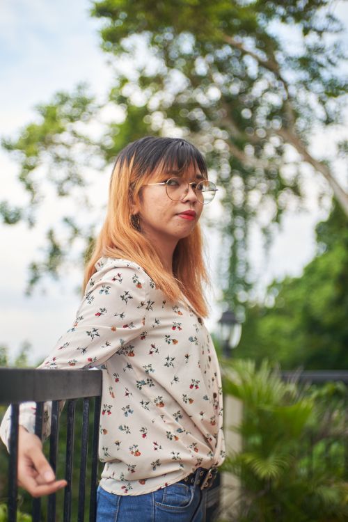 Free Casual portrait of a woman with glasses leaning against a railing in a park. Stock Photo