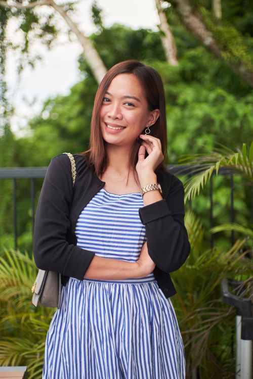 Free A confident young woman poses outdoors in a striped dress with vibrant greenery in the background. Stock Photo