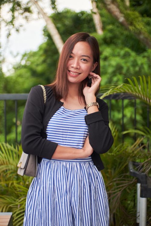 Free Portrait of a smiling woman in a striped dress and jacket, set against a lush green outdoor background. Stock Photo