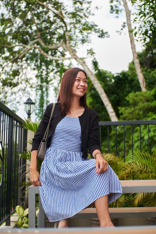 Free Asian woman smiling and sitting on a bench in a lush park setting. Stock Photo