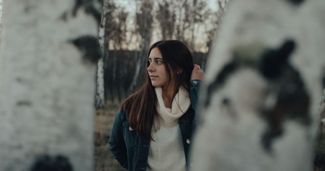 A young woman poses thoughtfully in a birch tree forest during daytime.