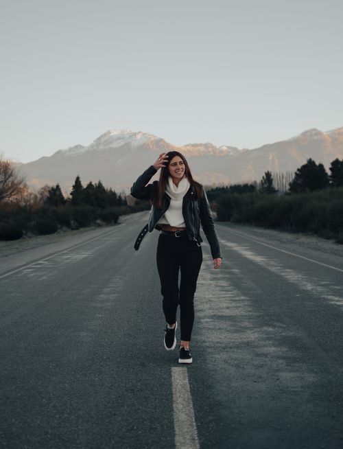 Free A woman walks confidently on a deserted road with mountains in the background, capturing a serene moment at dusk. Stock Photo