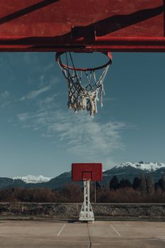 Rustic outdoor basketball hoop with mountains under clear sky.