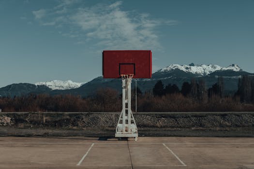 A solitary basketball hoop stands against a stunning mountain landscape under a clear sky.
