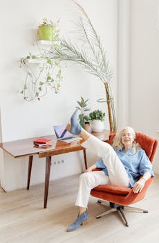 Senior woman enjoying leisure time in a stylish, modern home office setting with plants.