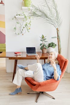 Elderly woman in a modern office chair, enjoying a relaxing moment near her workspace with plants.
