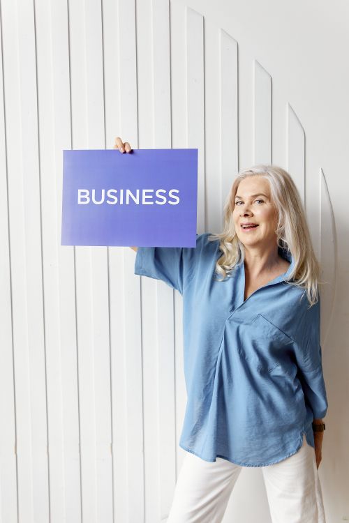 Free Senior woman smiling and holding a business sign against a modern white background. Stock Photo