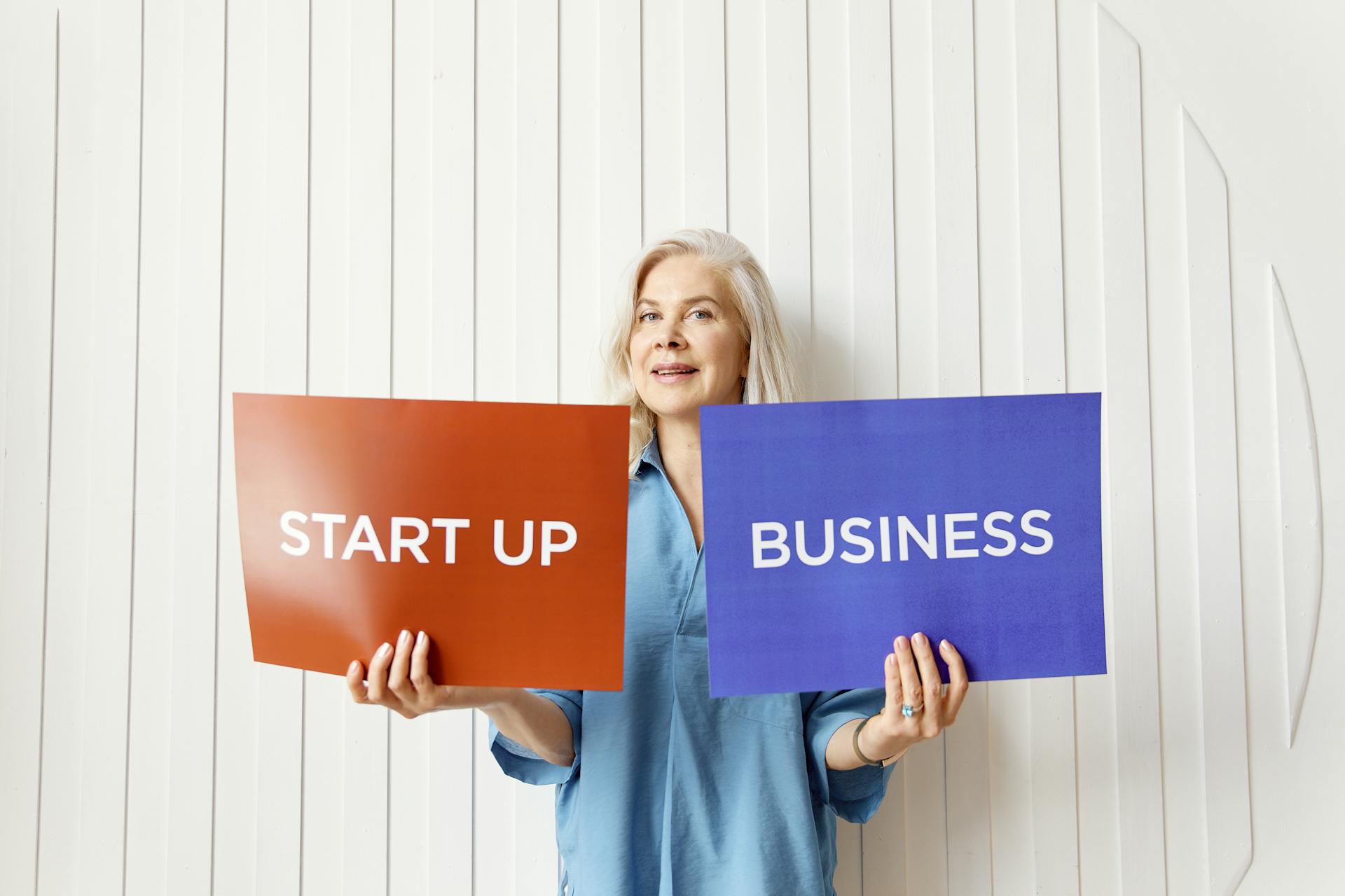 Elderly woman holding startup and business signs indoors against white background.