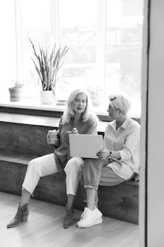 Monochrome image of two women discussing work with a laptop.