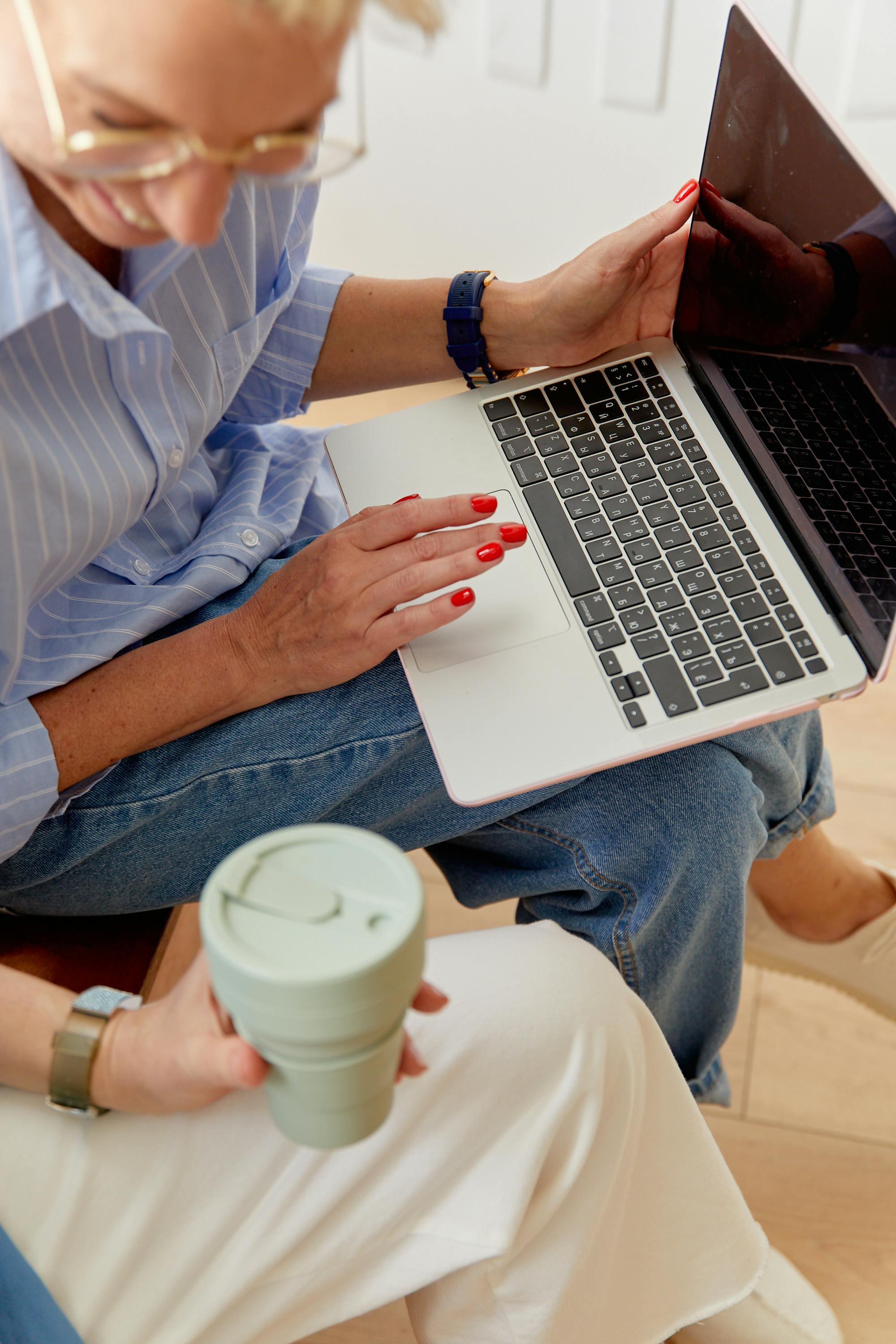 Close-up of a businesswoman using a laptop and holding a reusable cup, showcasing productivity.