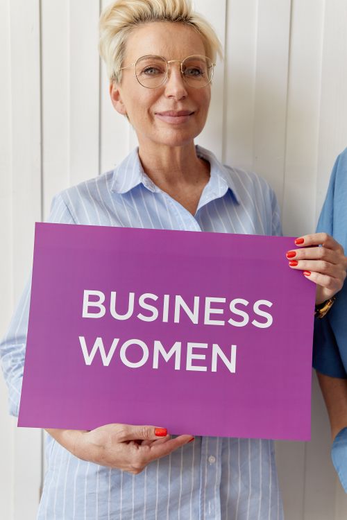 Free Confident businesswoman with eyeglasses holding a purple sign reading 'Business Women'. Stock Photo