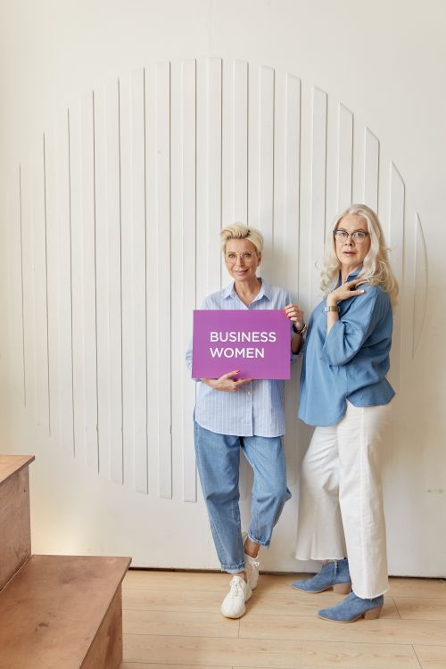 Free Two business women standing indoors, holding a purple business sign with confidence. Stock Photo