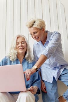 Two adult women working together on a laptop in a casual office environment with teamwork and cooperation.