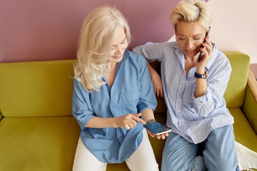 Free Two senior women with smartphones enjoying a digital communication moment on a stylish couch. Stock Photo