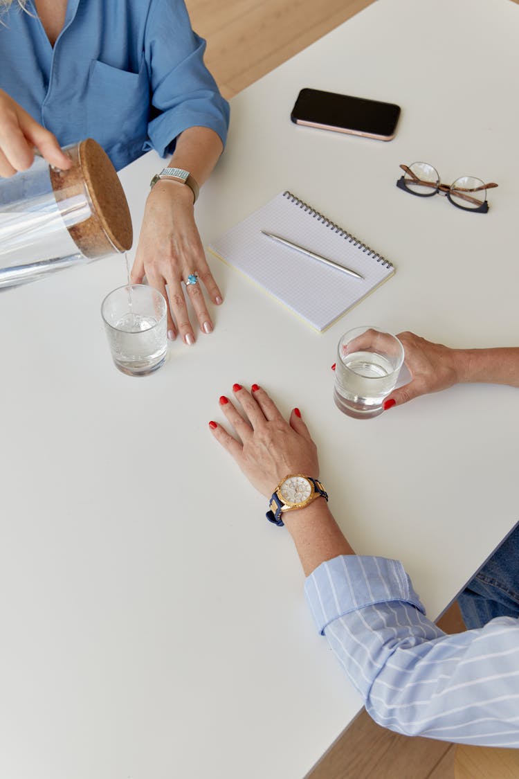 Glasses Of Water On White Table Between Women