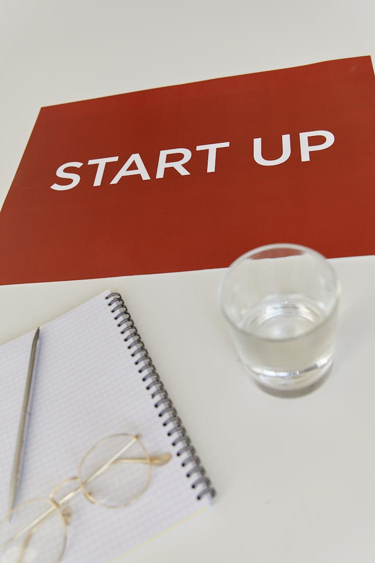 Red Poster Lying On Table By Notebook And Glass Of Water