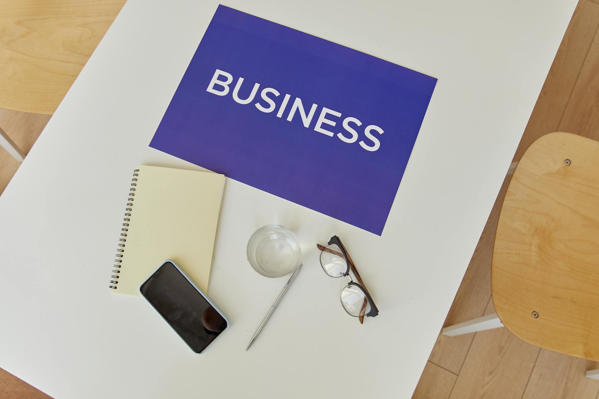 Top view of a minimalist business workspace with essentials like notebook, phone, glasses, and a business sign.