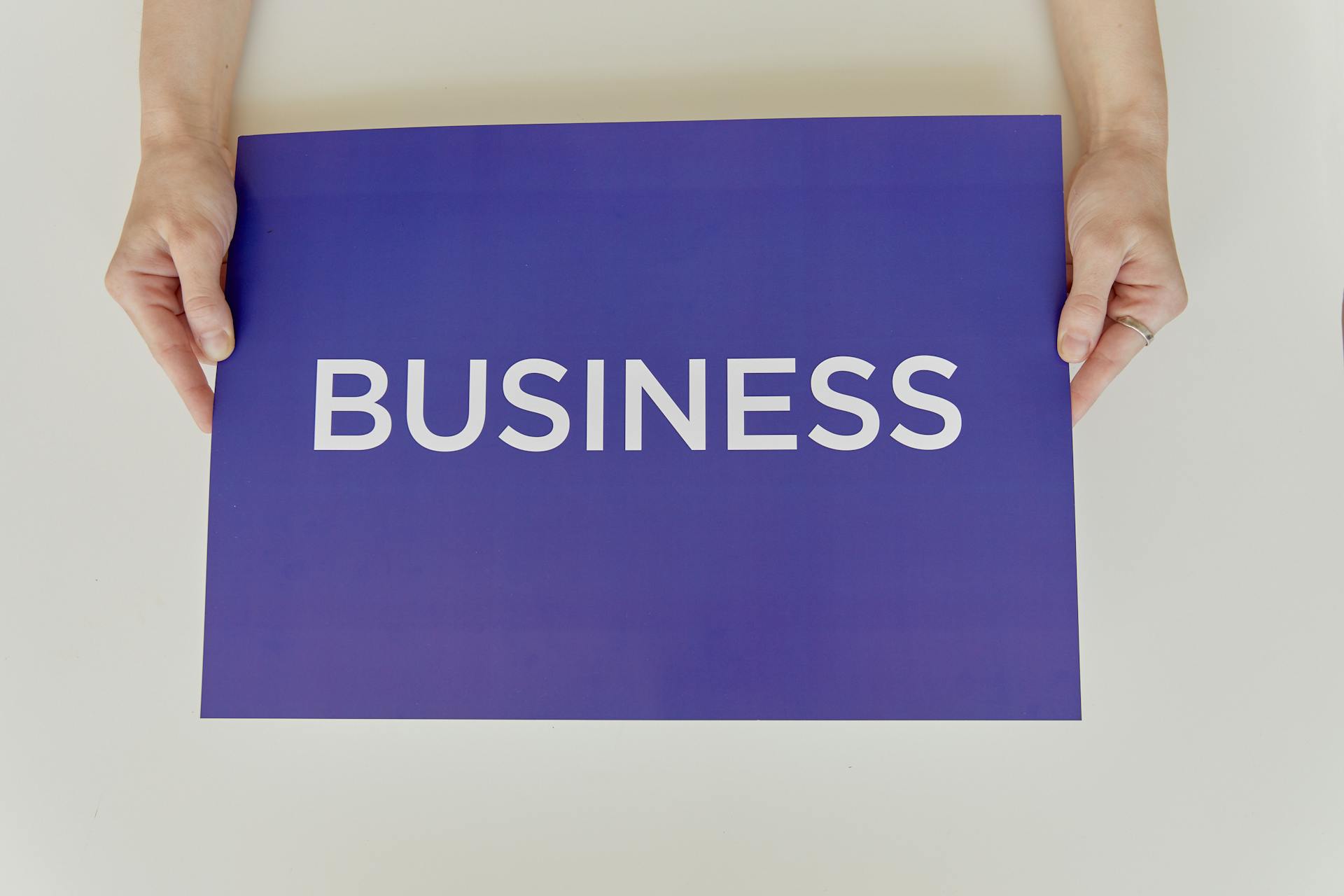 Hands holding a purple sign with the word 'BUSINESS', symbolizing corporate concepts.