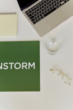 Minimalist office desk with laptop, glasses, and green brainstorming poster for fresh ideas.