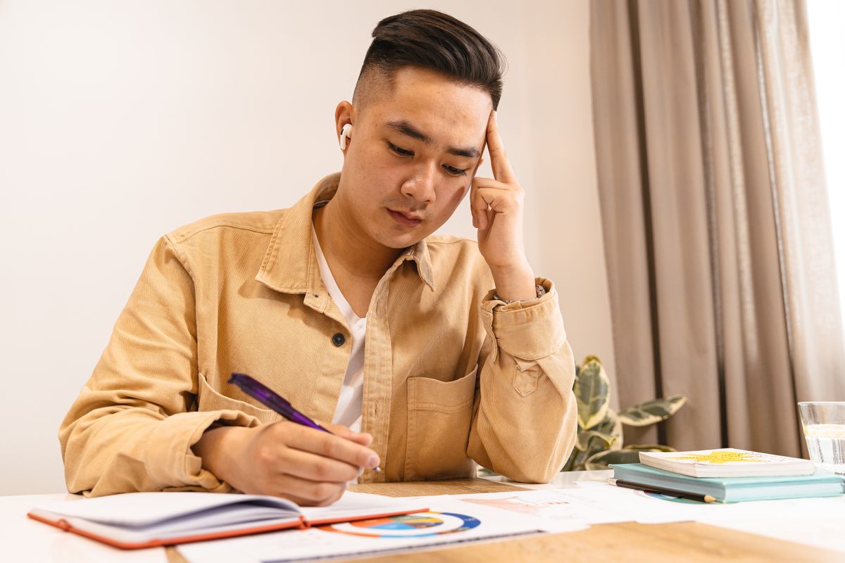 Student studying at a desk with earphones and writing notes in a notebook