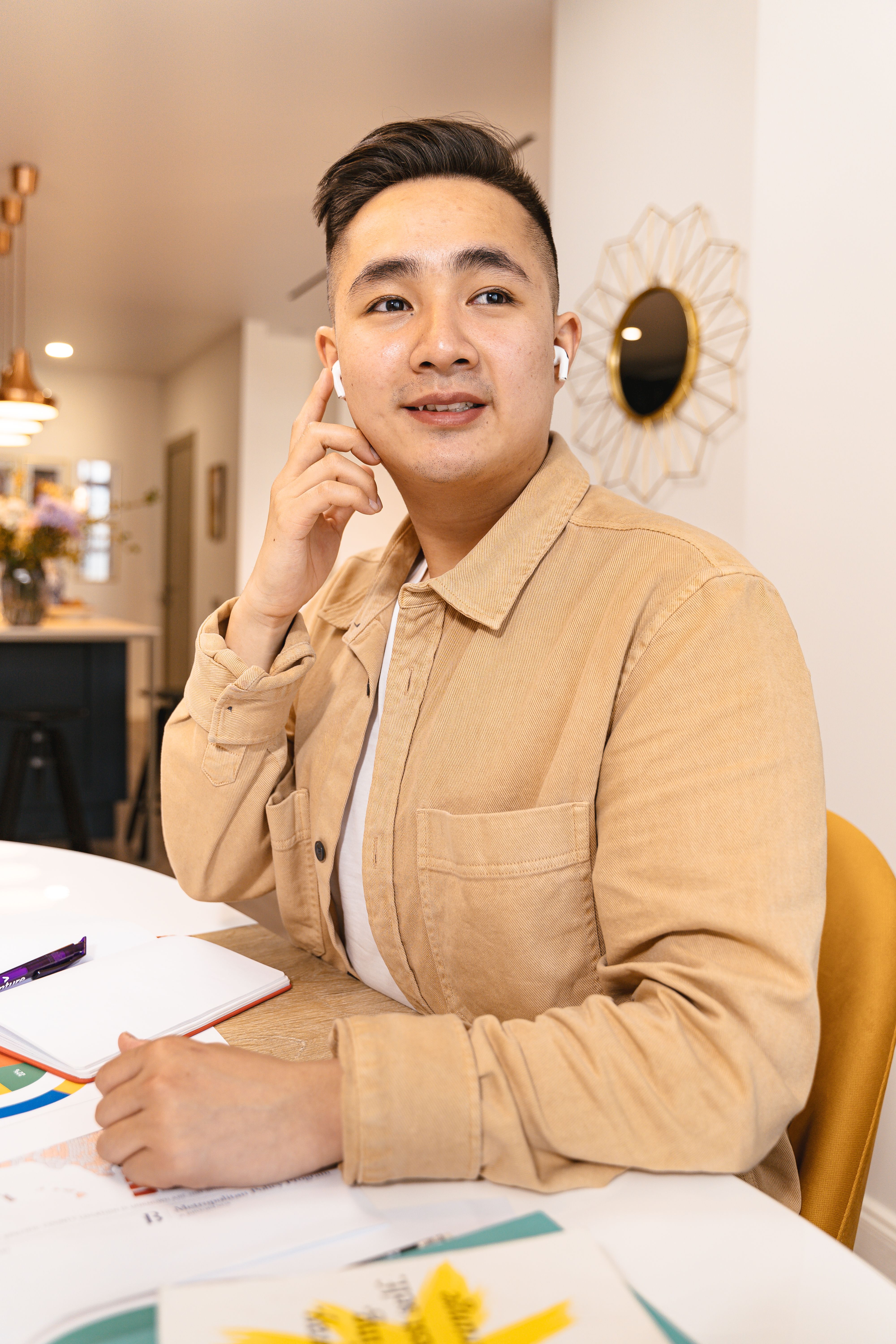 Asian man engaged in remote work using wireless earbuds in a casual office environment.