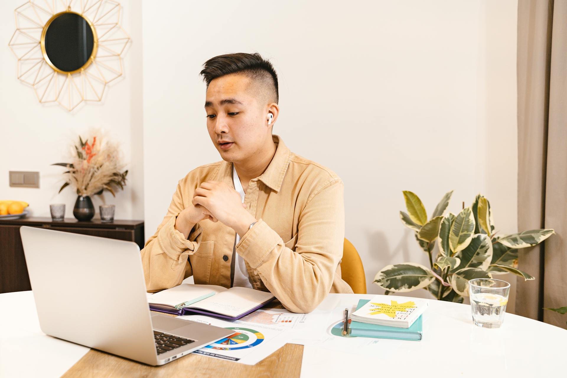 Asian man in casual wear attending an online meeting from home using a laptop.