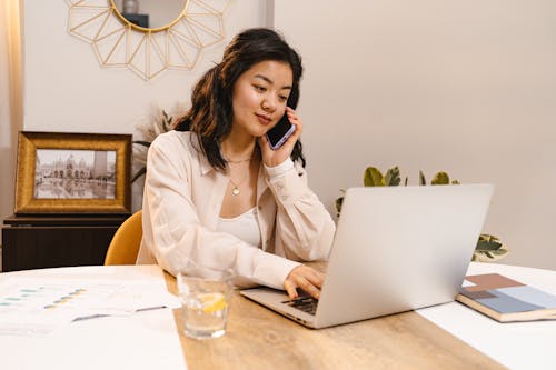Free A Woman Talking on the Phone while Using Her Laptop Stock Photo