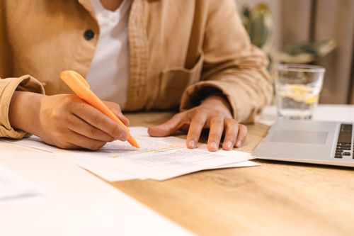 Free Person highlighting notes at a desk with a laptop and glass of water nearby. Stock Photo