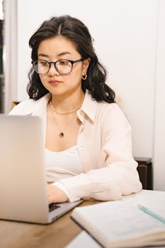 Asian businesswoman working on a laptop indoors, embodying the digital nomad lifestyle.