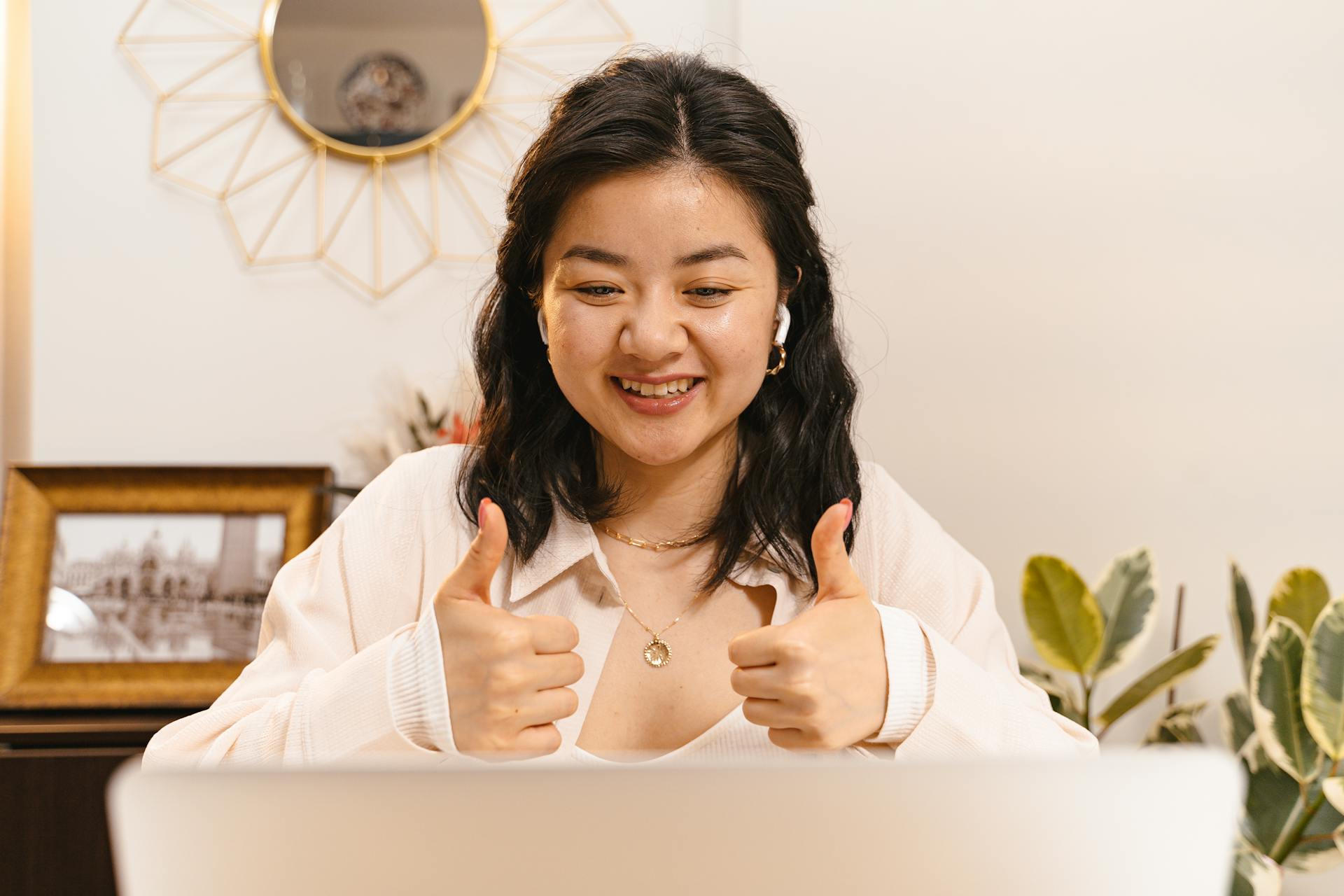 Asian businesswoman giving thumbs up during a successful online meeting, smiling and engaged.