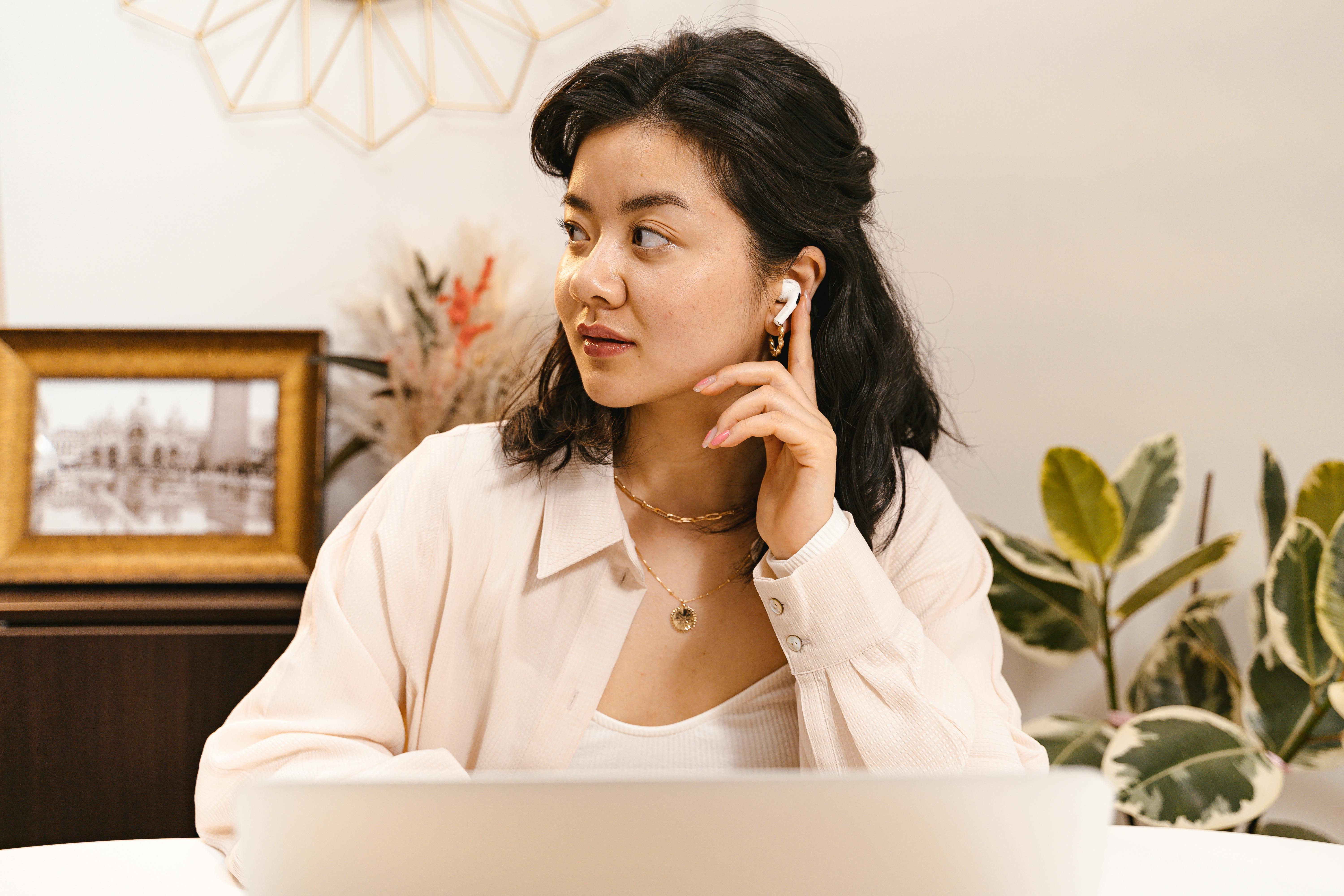 a woman in white long sleeves with gold necklace and airpods on her ear