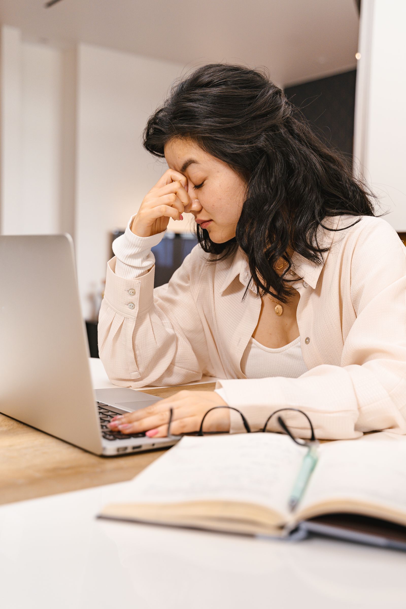 A woman at a laptop with her eyes closed and a hand to her temple