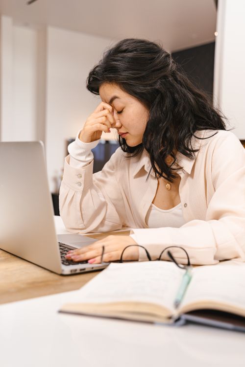 Free Woman with closed eyes feeling frustration while working on a laptop indoors. Stock Photo