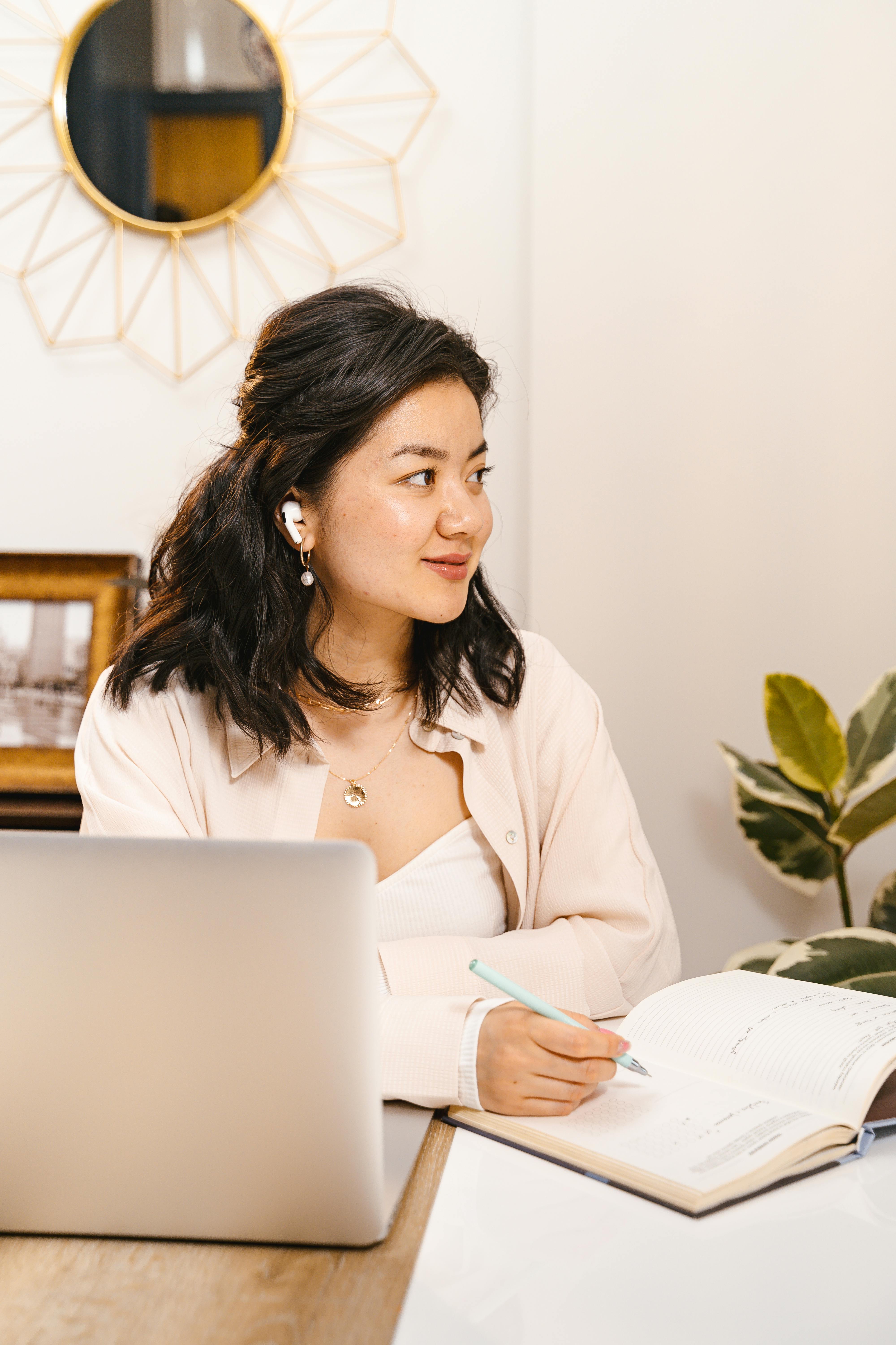 Focused woman writing notes at a desk with laptop, wearing earphones, and engaged in work.
