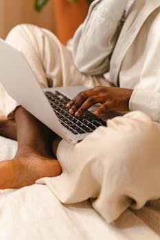 Person sitting cross-legged on bed using laptop, conveying comfort and focus.