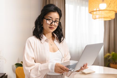 Free A confident woman with eyeglasses using a laptop in a modern home office setting. Stock Photo