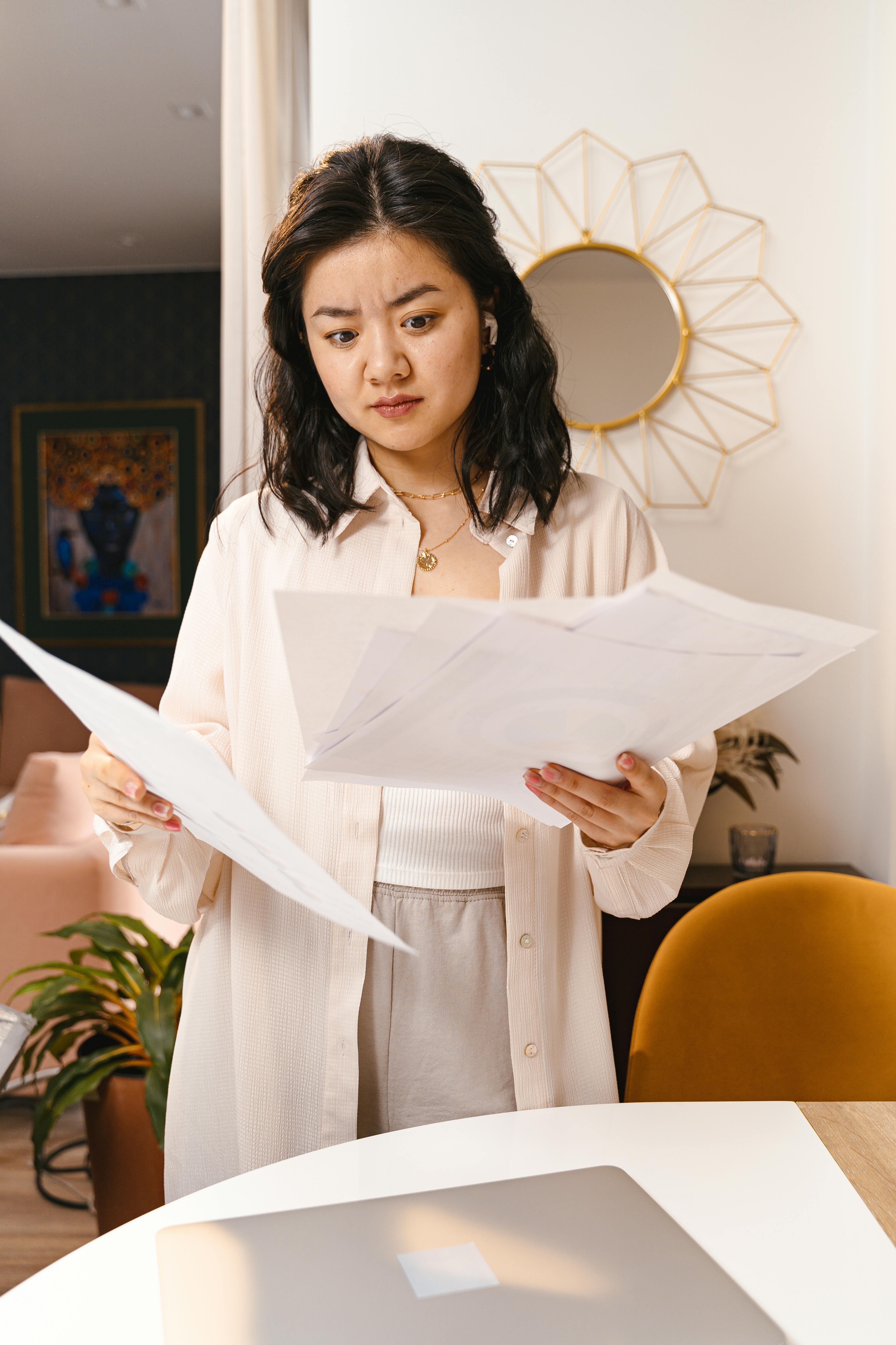 Young woman looks confused while reviewing documents in a modern home interior.