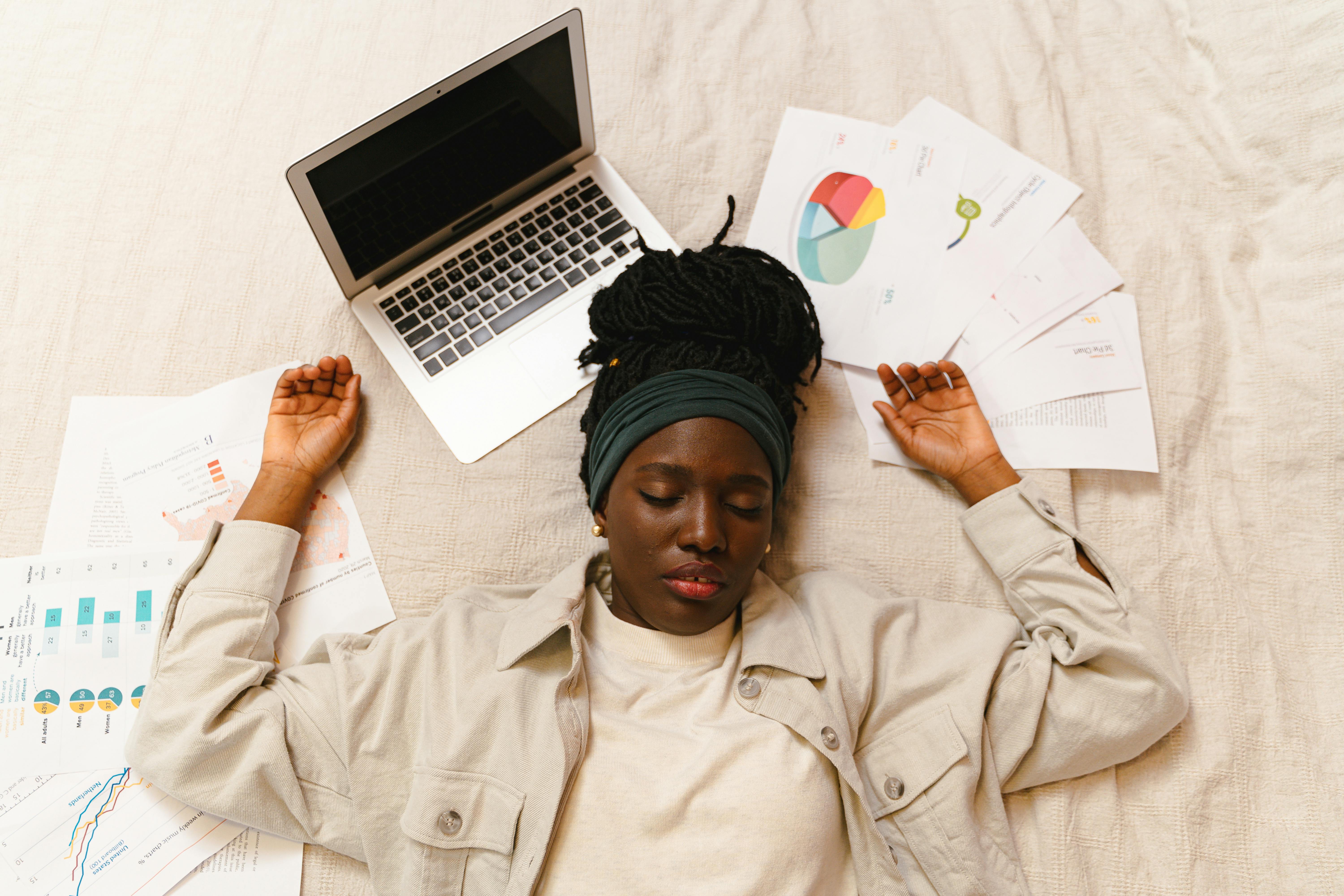 Tired woman with closed eyes lying by laptop and papers after work.