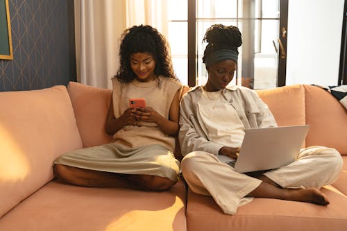 Women Sitting on the Couch while Using Mobile Phone and Laptop